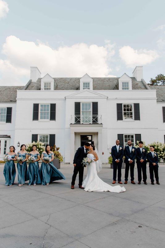 The bride and the groom share a heartfelt moment of love with the bridesmaids and the groomsmen in front of the mesmerizing Harding Waterfront Estate